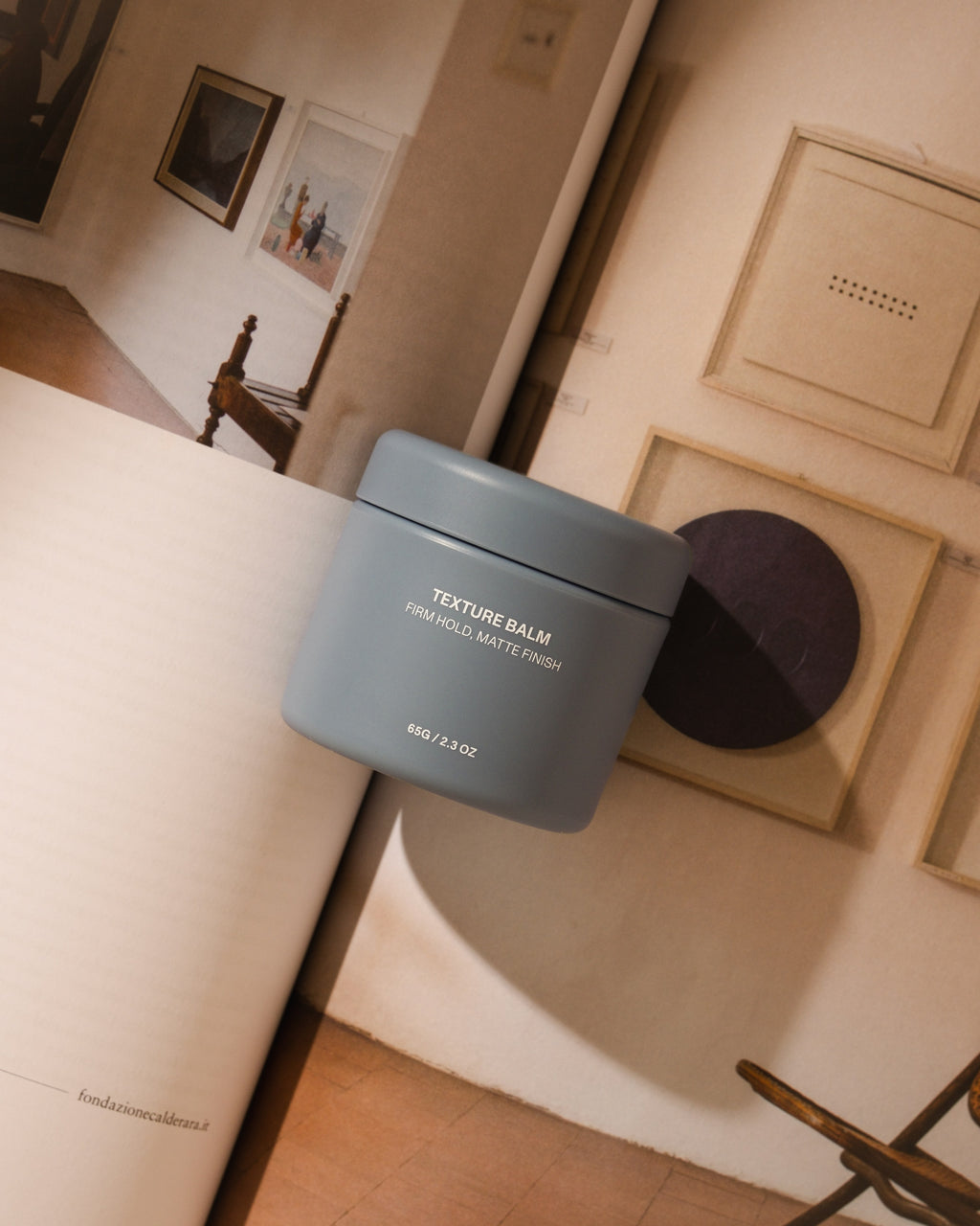 Blue Hairsauce Texture Balm cylindrical jar on an architectural book with natural tones