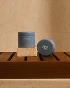 Two blue Hairsauce Texture Balm cylindrical jars on a wooden surface against a beige marble wall
